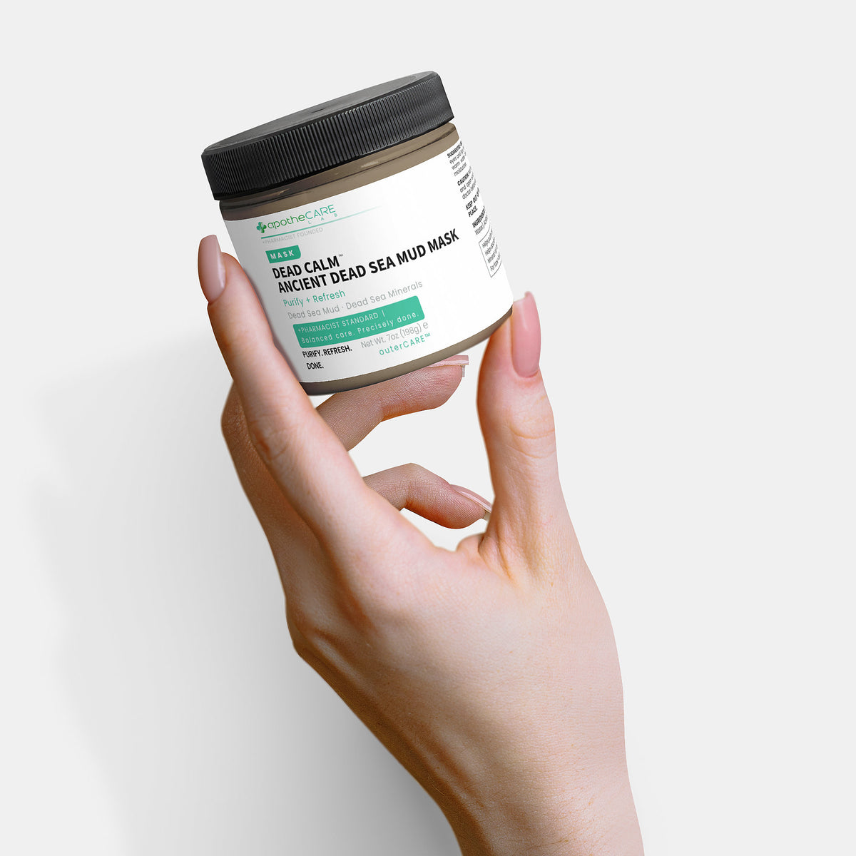 Hand holding a jar of Dead Calm Ancient Dead Sea Mud Mask against a white background