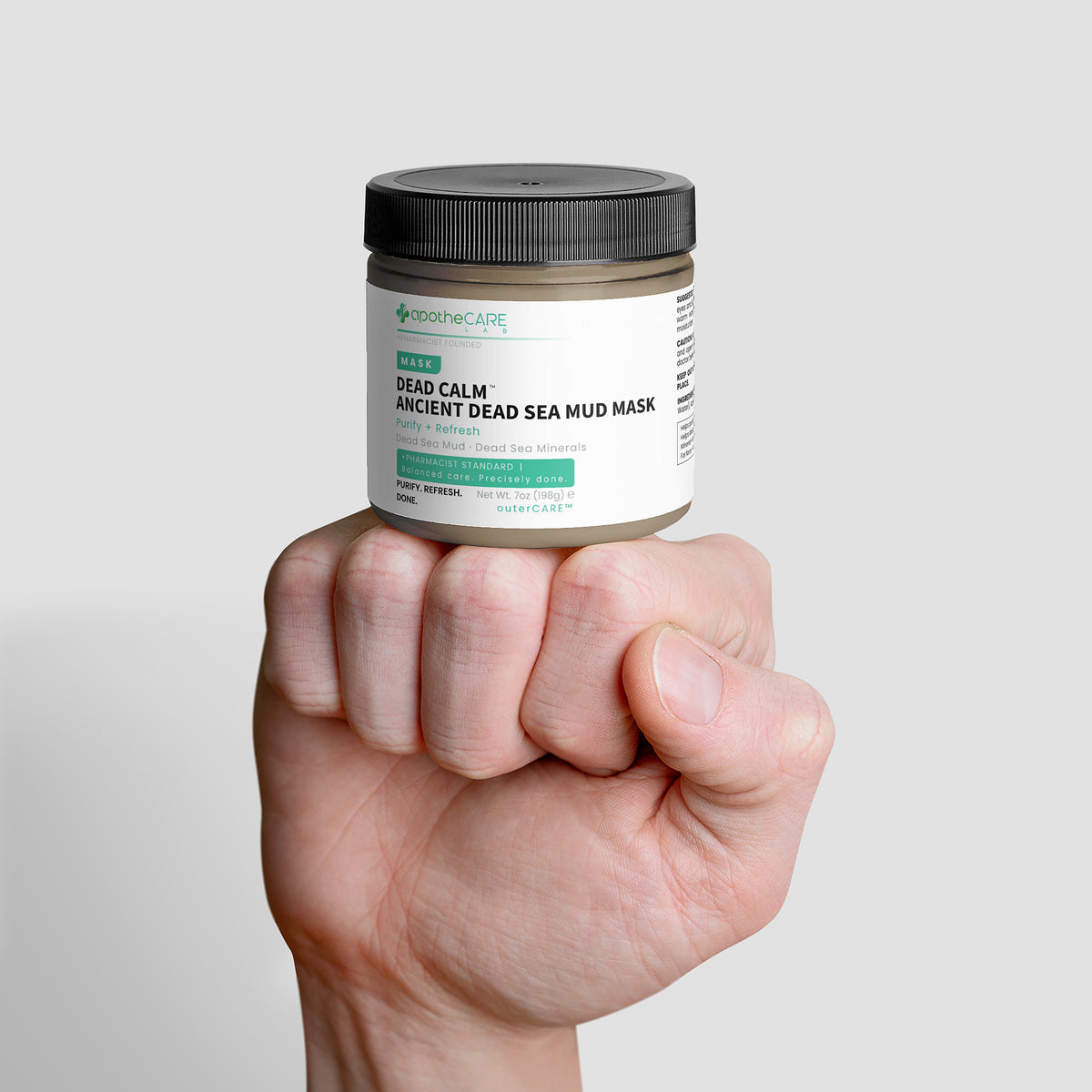 Hand holding a jar of 'Dead Calm Ancient Dead Sea Mud Mask' against a light gray background