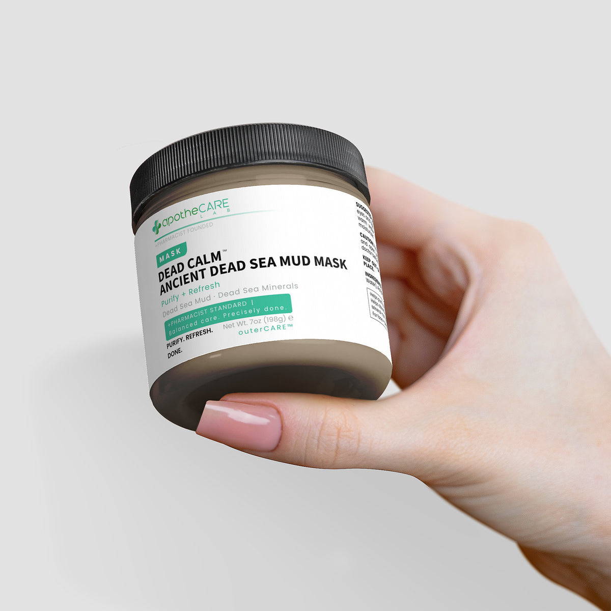 Hand holding a jar of 'Apothecare' Dead Sea Mud Mask against a light gray background