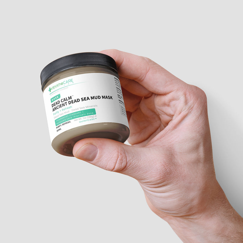 Hand holding a jar of Dead Sea Mud Mask with a plain background