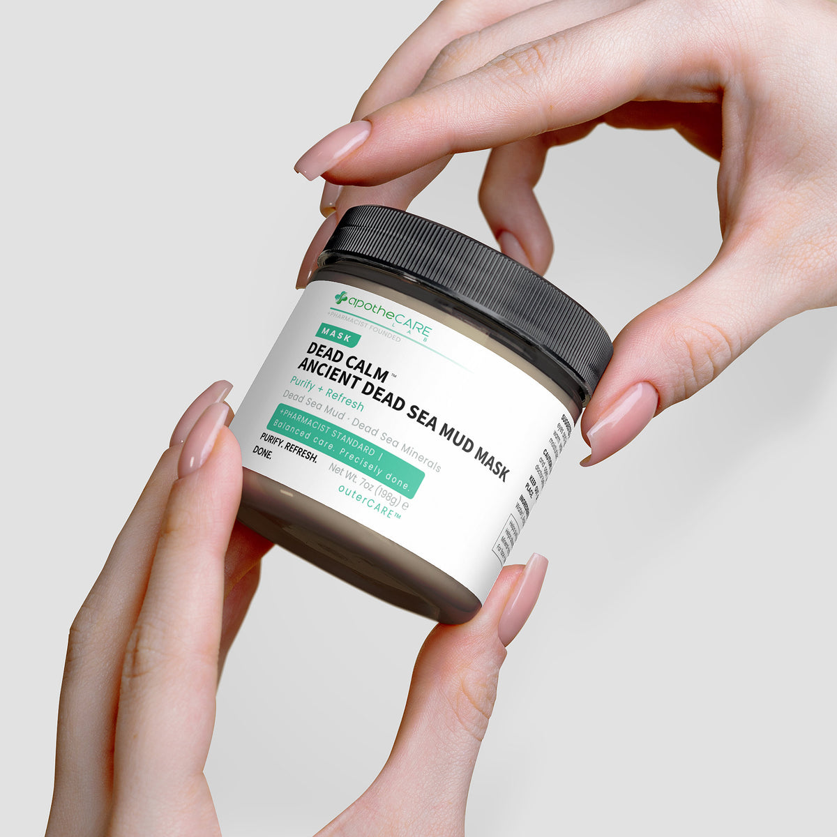 Hands holding a jar of  Dead Sea Mud Mask against a neutral background