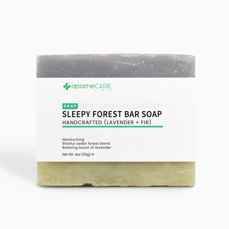 A bar of soap labeled 'apothecare lab Sleepy Forest Bar Soap' with a white paper label, showing a dark gray top half and a pale yellow-green bottom half, on a light gray background.