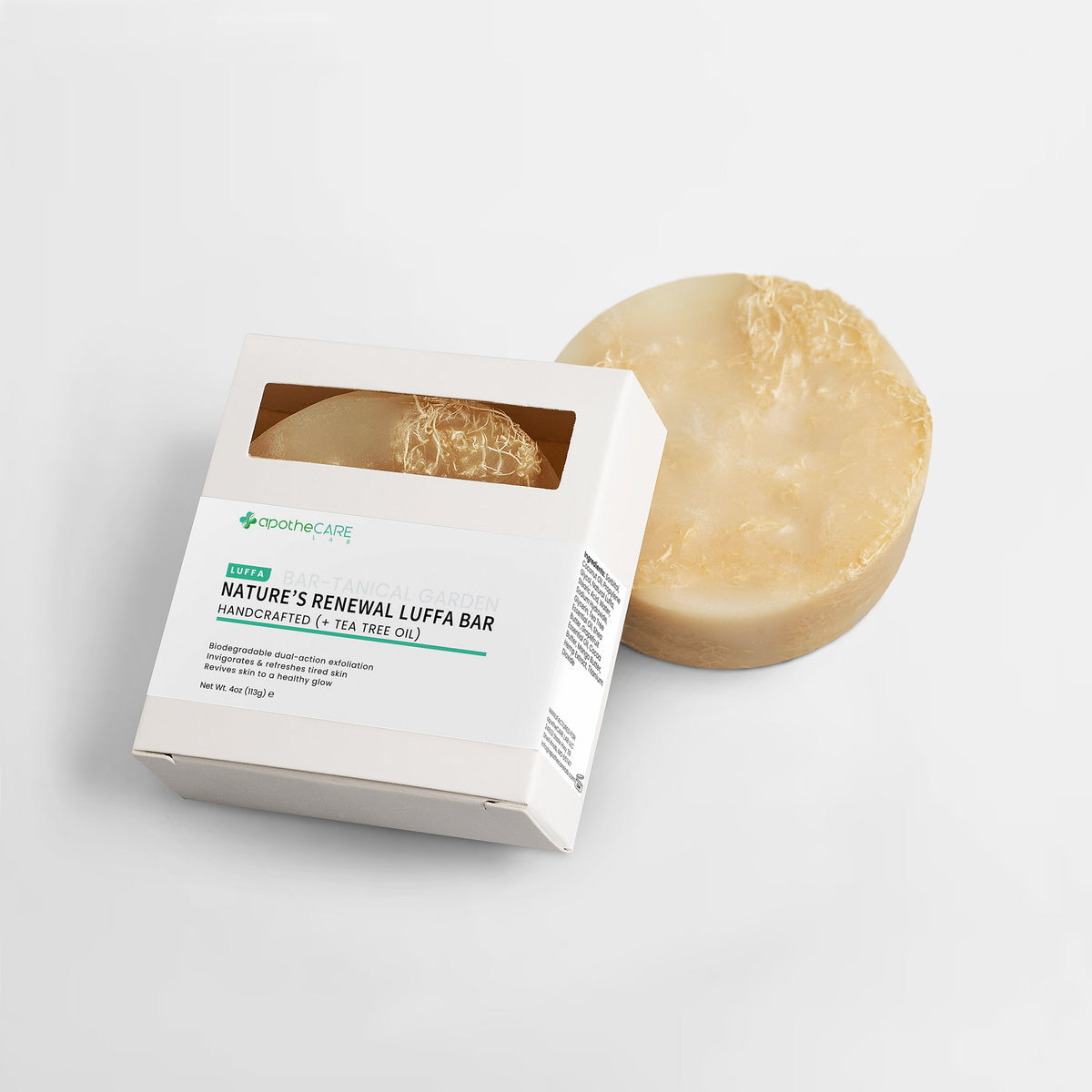 A round natural beige handcrafted luffa bar soap sits behind its white cardboard packaging box, which features a clear window showing the textured soap inside. The box is labeled 'NATURE'S RENEWAL LUFFA BAR'.