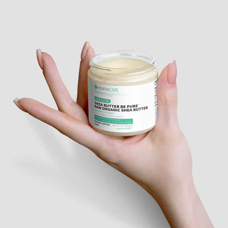A hand holding an open jar of Shea Butter against a light gray background.