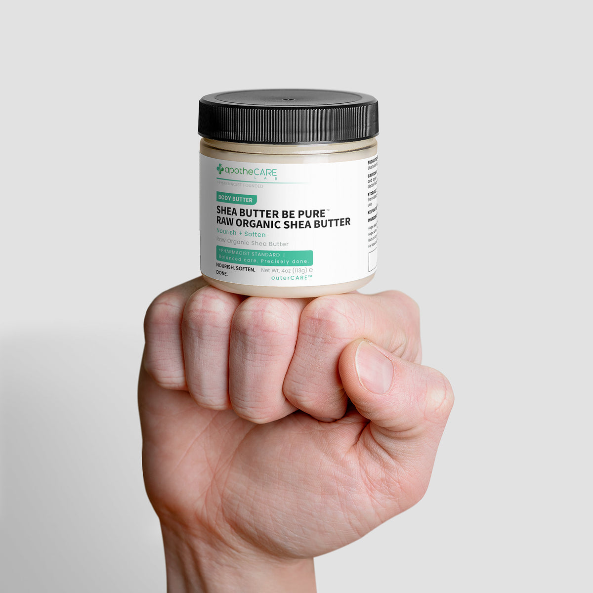 Hand holding a jar of organic shea butter against a plain background
