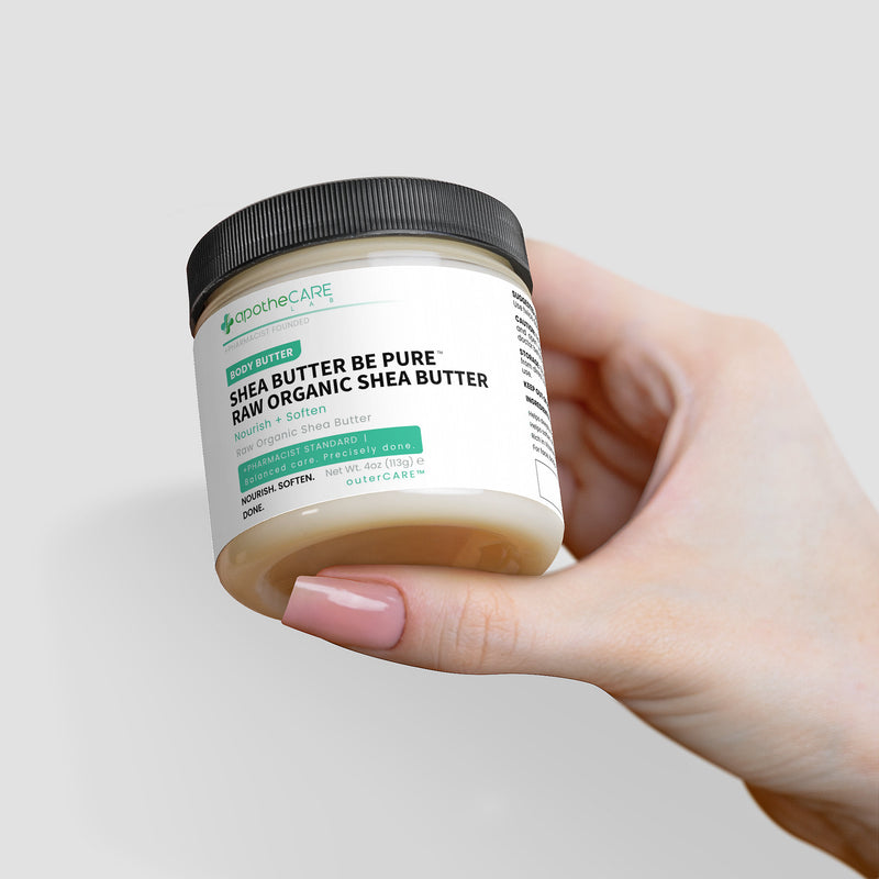 A hand holding a jar of apotheCARE LAB Raw Organic Shea Butter against a light gray background.