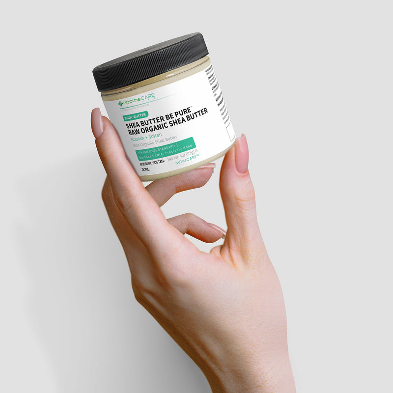 A hand holding a jar Shea Butter Be Pure Raw Organic Shea Butter against a light gray background.