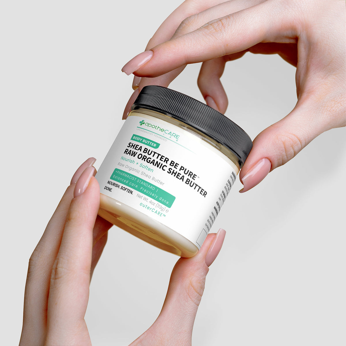 Jar of shea butter held by hands with a plain background