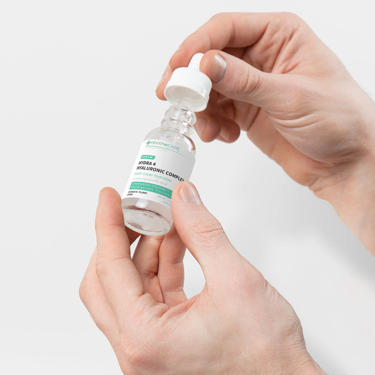 A person's hands holding and unscrewing the cap of a small clear glass dropper bottle of Hyaluronic Serum on a light gray background.