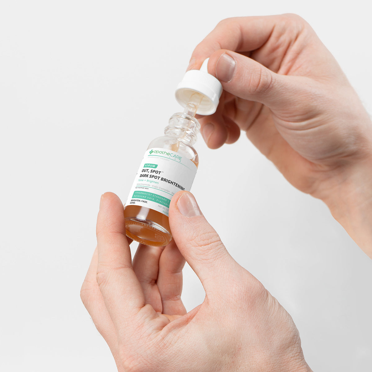 Hand holding a bottle of 'Out, Spot.' dark spot serum with a dropper.