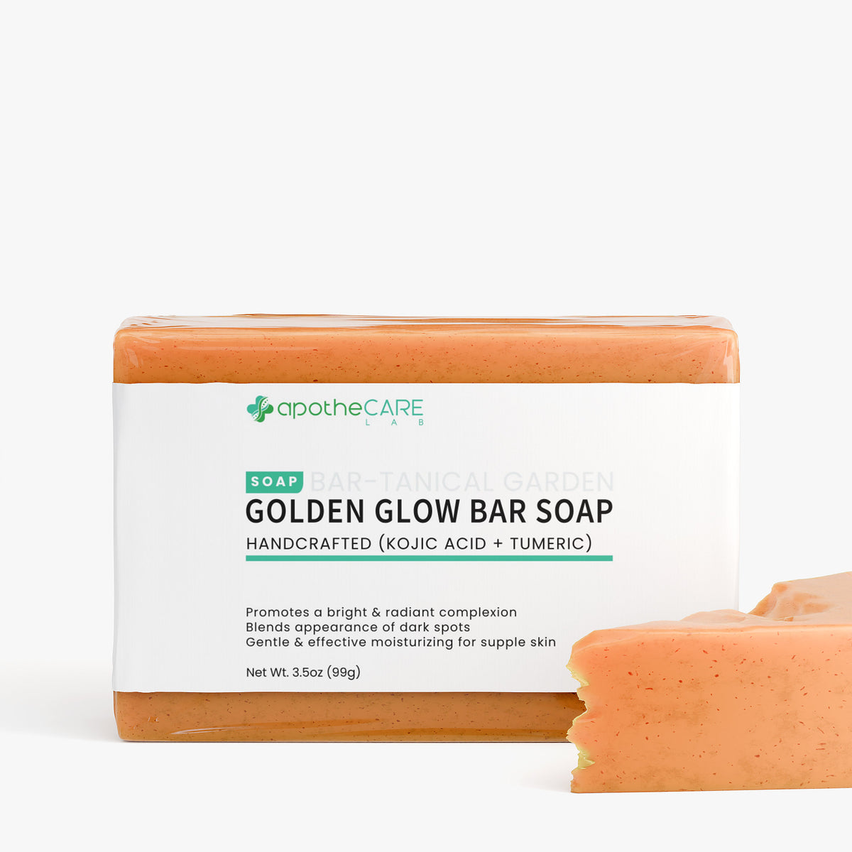 A bar of ApotheCare Gold Glow Bar Soap with its white paper label wrapper, shown on a clean white background with a small broken piece of the soap in the foreground.