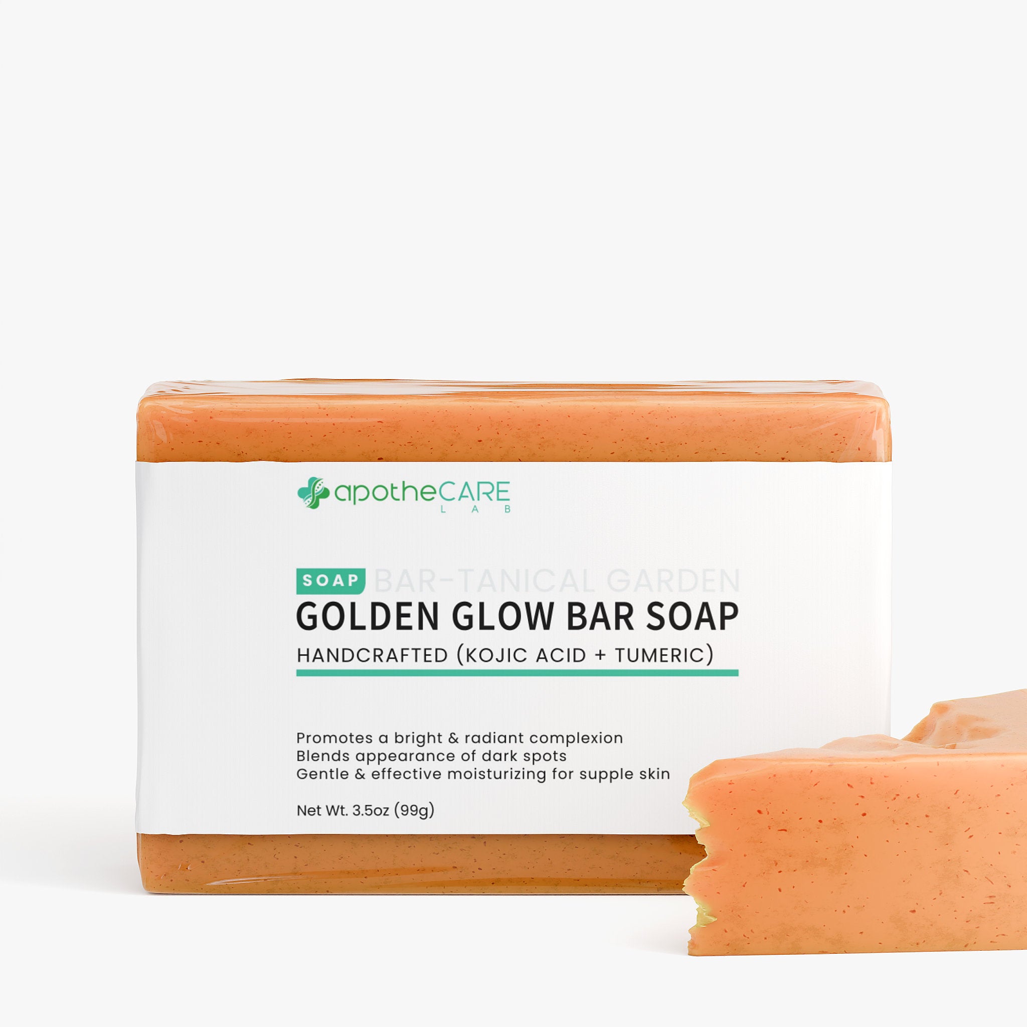 A bar of ApotheCare Gold Glow Bar Soap with its white paper label wrapper, shown on a clean white background with a small broken piece of the soap in the foreground.