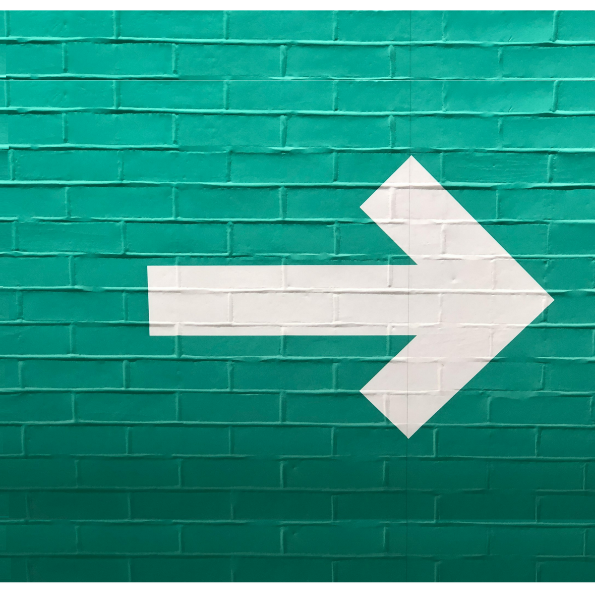 White arrow on a teal brick wall