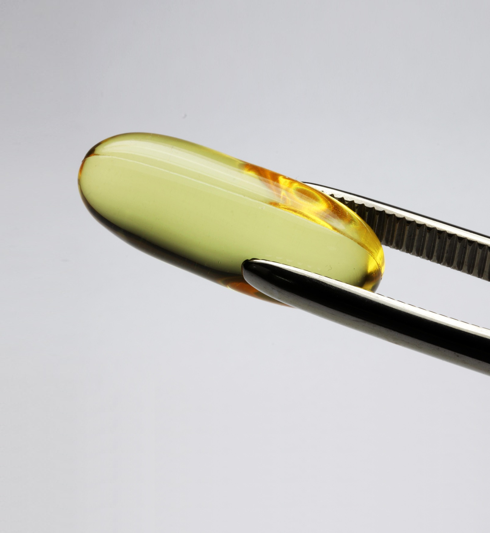 Yellow capsule on tweezers against a gray background