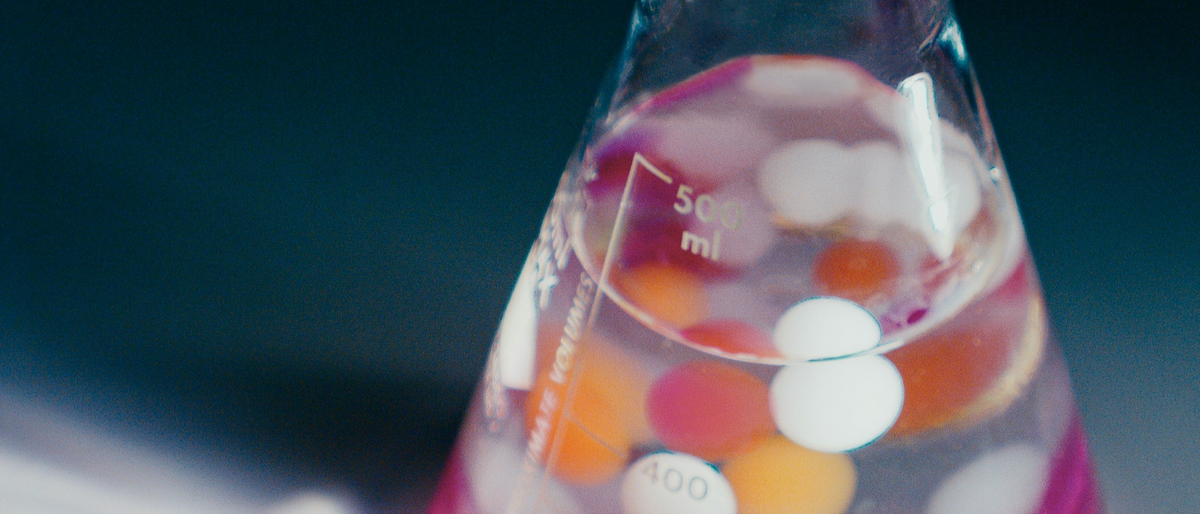 Erlenmeyer flask with colorful liquid and white spherical objects on a dark background