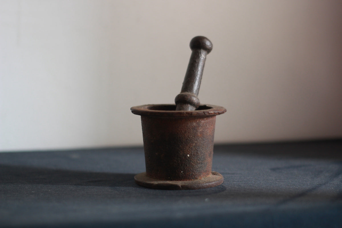 Old rusted metal mortar and pestle on a black dusty table.