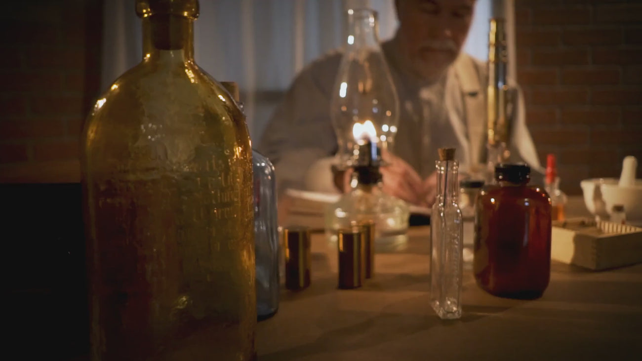 older gentleman writing in a book with an old ink pen surrounded by old medicine bottles
